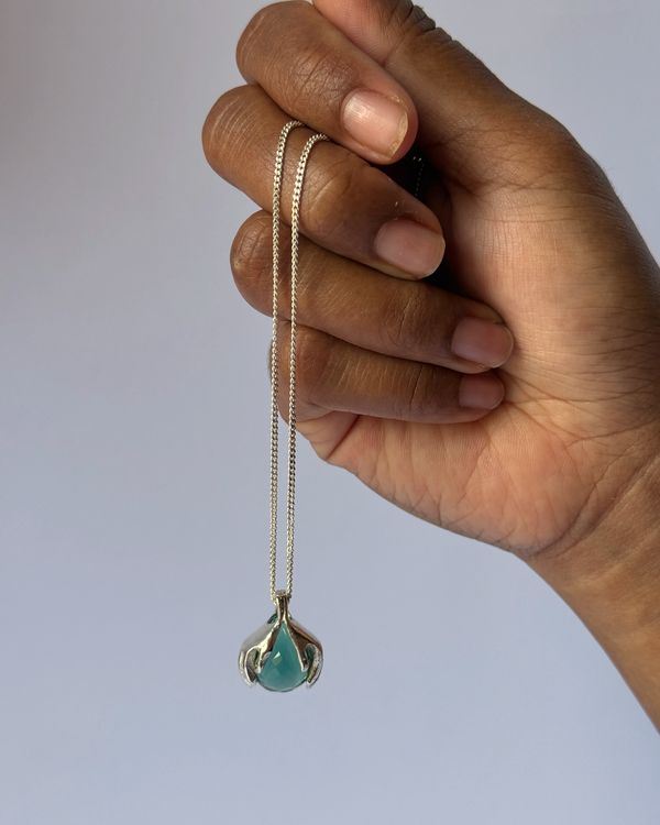 A hand holding the Rona pendant by its chain